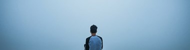 boy sitting on hill looking out into a misty landscape